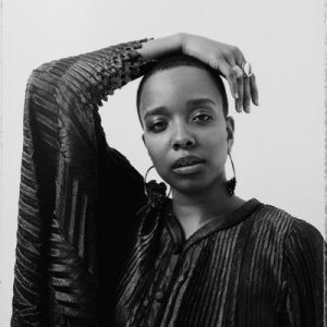 Black and white photo of Jamila Woods posing with her hand resting atop her head.